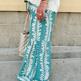 Lightweight printed wide-leg pants with a tropical pattern in dusty blue and cream tones, featuring a drawstring waist and pockets.