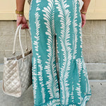 Lightweight printed wide-leg pants with a tropical pattern in dusty blue and cream tones, featuring a drawstring waist and pockets.