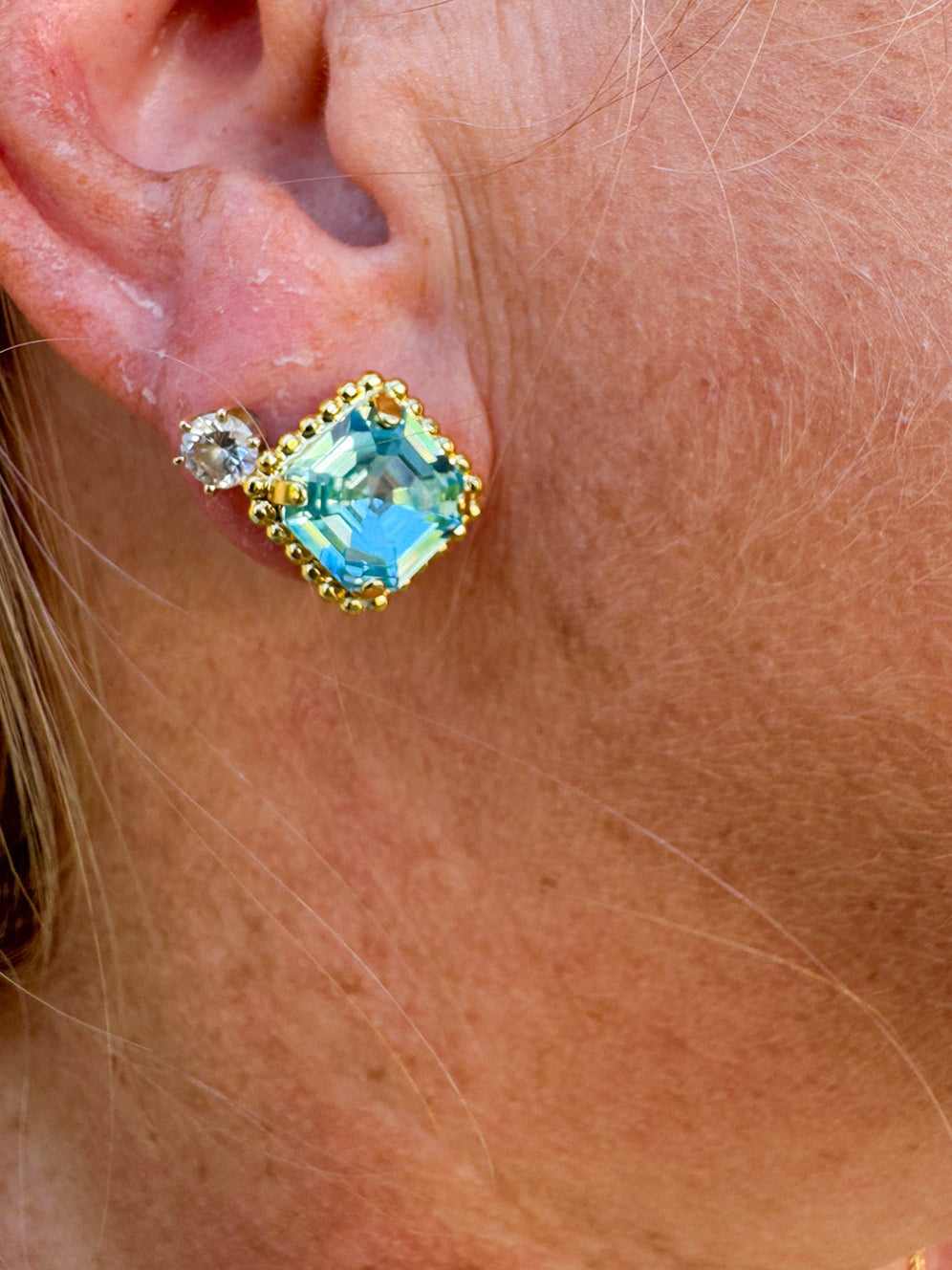 Bright gold-tone stud earrings with aquamarine square-cut crystals and a metal beaded halo from Sorrelli’s Aquamarine Collection.