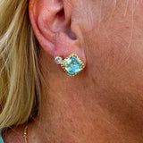 Bright gold-tone stud earrings with aquamarine square-cut crystals and a metal beaded halo from Sorrelli’s Aquamarine Collection.