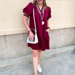 Garnet knee-length ruffle dress with puff sleeves, V-neckline, off-white contrast stitching, and ruffled hem.