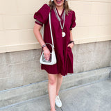 Garnet knee-length ruffle dress with puff sleeves, V-neckline, off-white contrast stitching, and ruffled hem.