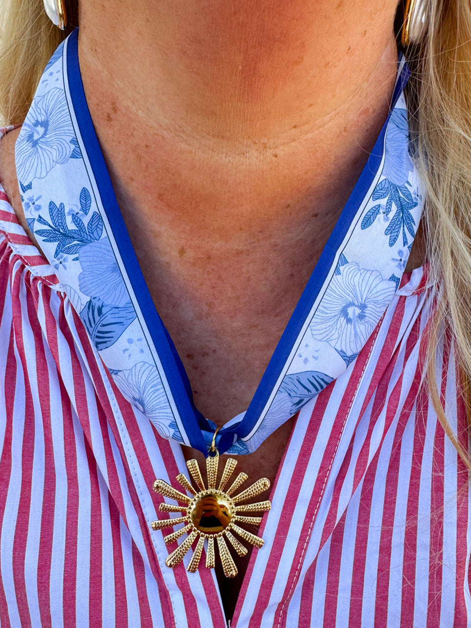 Blue and white floral fabric scarf necklace with a gold sunburst charm and tie-back design, styled as a lightweight statement accessory.