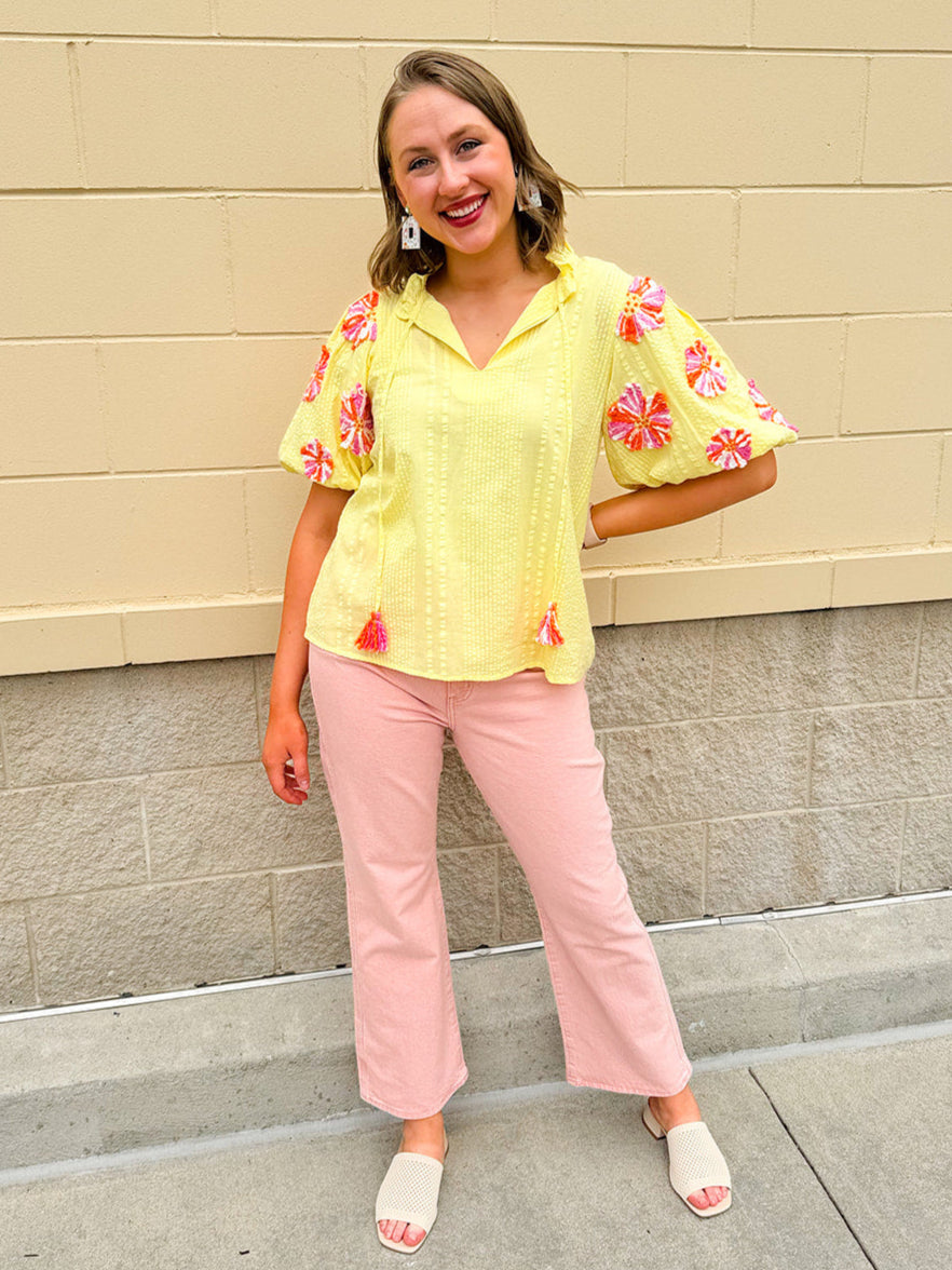 Yellow puff sleeve top with seersucker texture and 3D embroidered flowers in white, pink, and orange; ruffle collar and pom-pom tie details.
