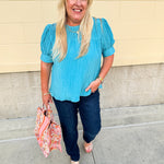 Light pink pleated top with puff sleeves and back tie details, styled for a breezy, feminine look.