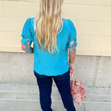 Light pink pleated top with puff sleeves and back tie details, styled for a breezy, feminine look.