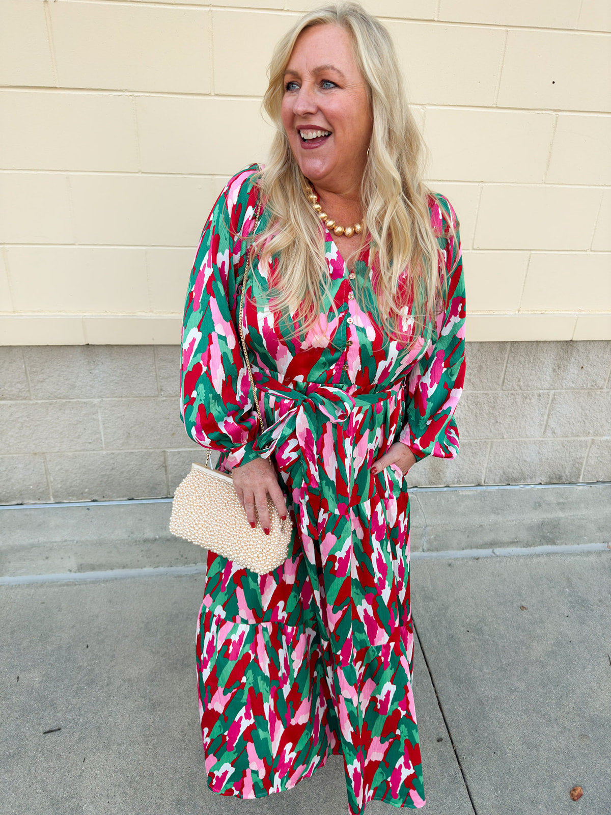 A feminine midi dress with ruffled neckline, long sleeves, and abstract floral print in red, pink, and green.