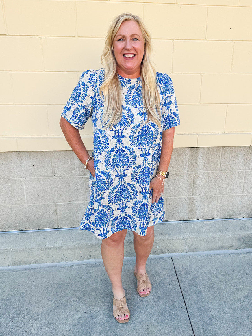 Blue and white damask print short-sleeve mini dress with pockets and back zipper closure, styled for a casual yet polished look.