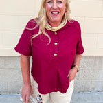 Garnet short sleeve button-up blouse with collar, cuffed sleeves, and gold statement buttons down the front.