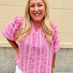 Pink cotton top with cream floral embroidery, ruffled v-neckline, and puff sleeves