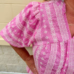 Pink cotton top with cream floral embroidery, ruffled v-neckline, and puff sleeves