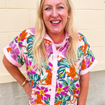 Women’s colorful tropical print button down top with leopards, pink and orange flowers, green leaves, blush pink collar, and short cuffed sleeves.