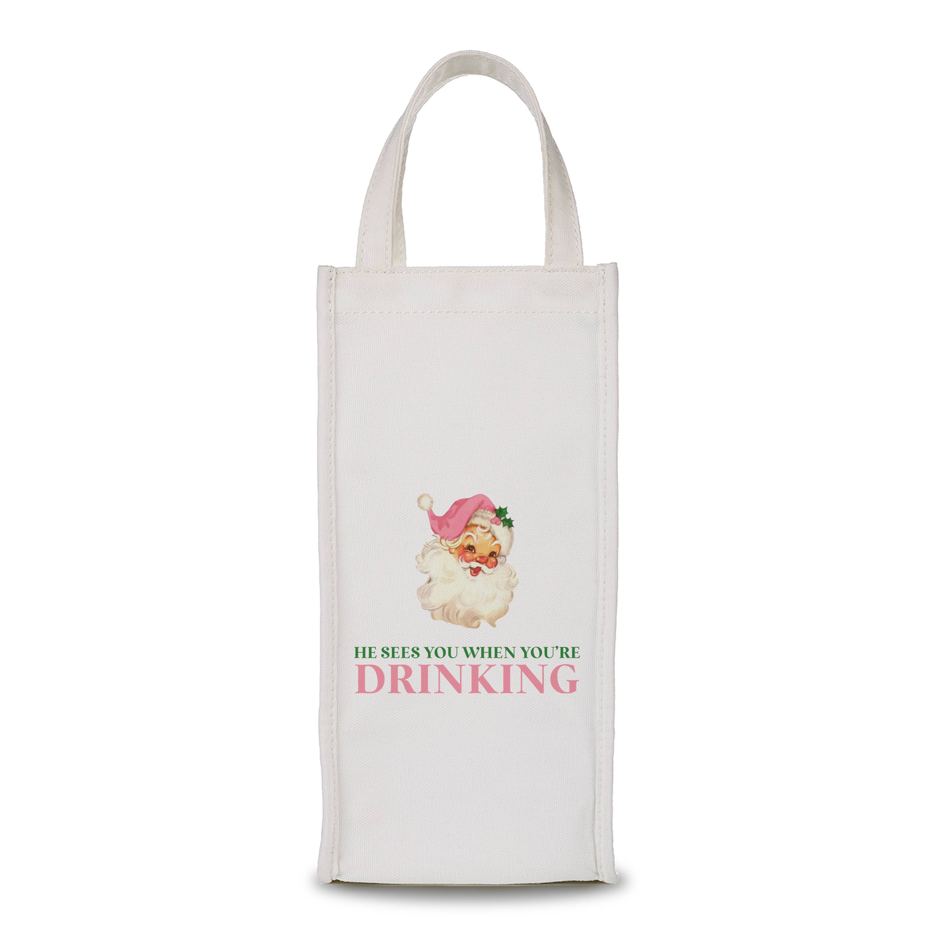 White fabric wine bag with Santa head in pink hat and text reading “He Sees You When You’re Drinking.”