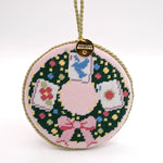 Round needlepoint mahjong ornament with wreath design, colorful mahjong tiles, bird, and pink bow.