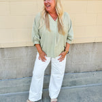 Sage green V-neck loose-fit blouse with pleated cuffed sleeves, styled for a fresh and effortless look.