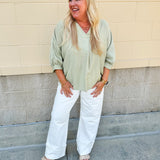 Sage green V-neck loose-fit blouse with pleated cuffed sleeves, styled for a fresh and effortless look.
