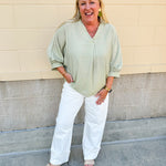 Sage green V-neck loose-fit blouse with pleated cuffed sleeves, styled for a fresh and effortless look.