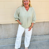 Sage green V-neck loose-fit blouse with pleated cuffed sleeves, styled for a fresh and effortless look.