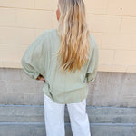 Sage green V-neck loose-fit blouse with pleated cuffed sleeves, styled for a fresh and effortless look.