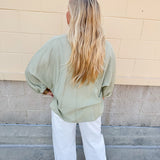 Sage green V-neck loose-fit blouse with pleated cuffed sleeves, styled for a fresh and effortless look.