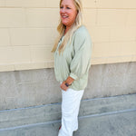 Sage green V-neck loose-fit blouse with pleated cuffed sleeves, styled for a fresh and effortless look.