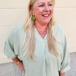 Sage green V-neck loose-fit blouse with pleated cuffed sleeves, styled for a fresh and effortless look.
