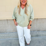 Sage green V-neck loose-fit blouse with pleated cuffed sleeves, styled for a fresh and effortless look.