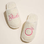 Plush fuzzy bridal slippers with “Bride” embroidery on one foot and pink diamond ring embroidery on the other, U.S. sizing M & L.