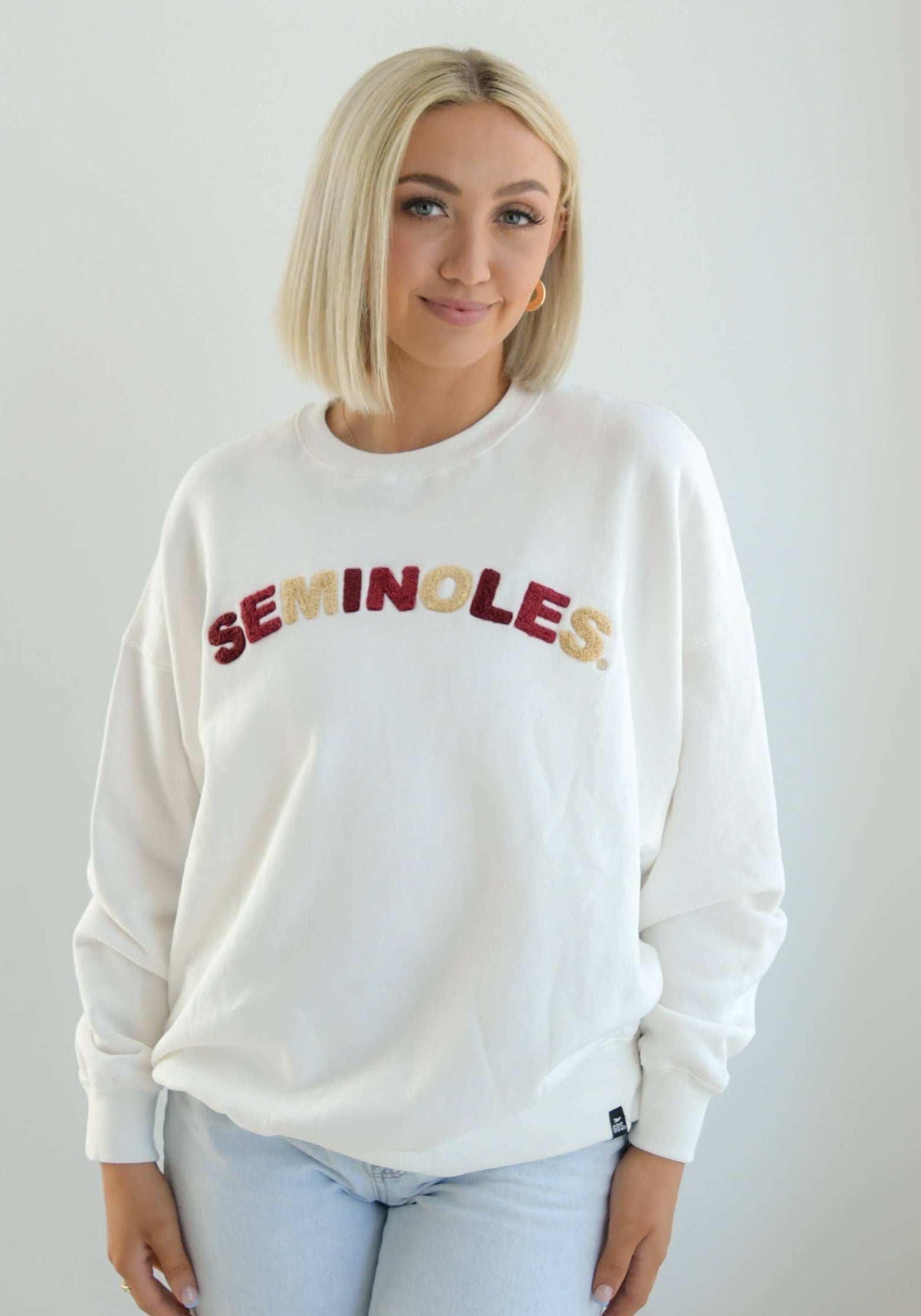 White cropped fleece crewneck sweatshirt with alternating garnet and gold chenille “Seminoles” lettering across the chest.