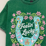 Green short sleeve graphic t-shirt with horseshoe design and “Feelin’ Lucky” text on the front with a relaxed casual fit.