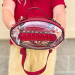 Clear football-shaped crossbody bag with garnet trim, zipper closure, and adjustable straps.