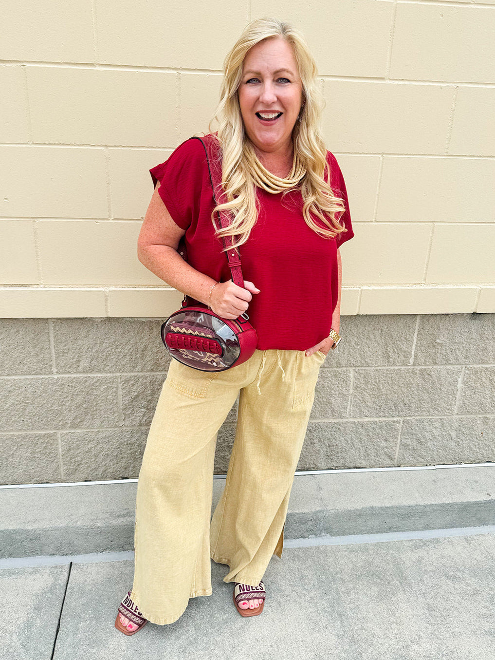 Clear football-shaped crossbody bag with garnet trim, zipper closure, and adjustable straps.