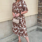 White dress with an allover brown leaf print featuring green details, button-down front, adjustable waist tie, and three-quarter-length sleeves