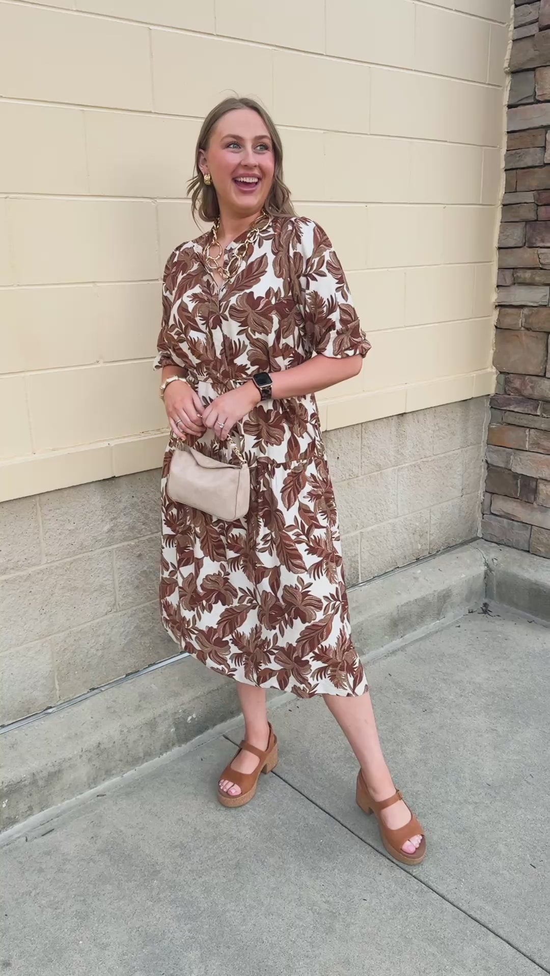 White dress with an allover brown leaf print featuring green details, button-down front, adjustable waist tie, and three-quarter-length sleeves