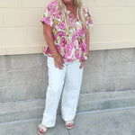 Pink floral babydoll top with ruffle collar, short sleeves, and a tie-neck detail, styled for a soft and feminine look.