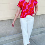 Banana and floral print top in orange and hot pink with V-neck and short dolman sleeves, displayed on hanger against neutral background