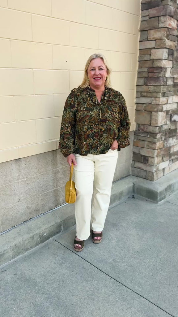 Spiced Botanical Blouse featuring a dark green base, intricate orange, red, green, and beige floral and swirl print, long sleeves, and a tie neckline.