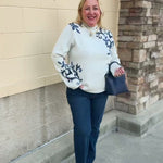 White long-sleeve mock-neck sweater with navy and light blue floral details on the shoulders and sleeves.