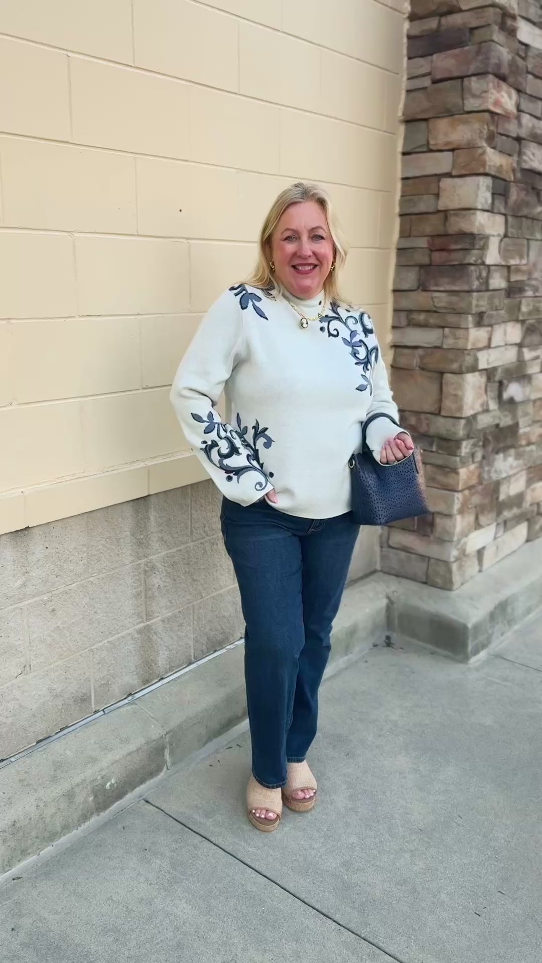 White long-sleeve mock-neck sweater with navy and light blue floral details on the shoulders and sleeves.