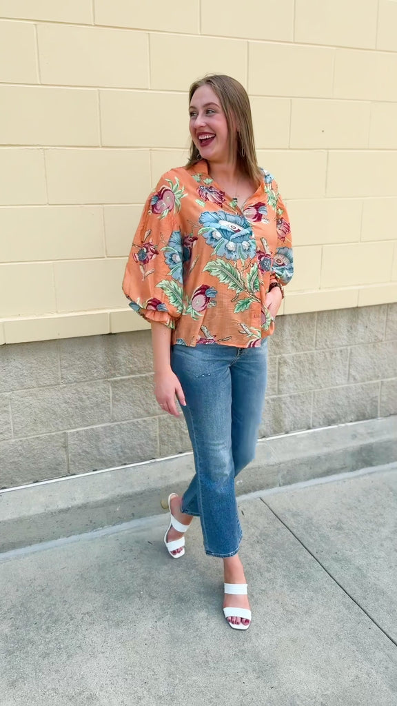 Woman wearing a vibrant coral balloon sleeve button-down top with gathered 3/4-length sleeves, styled in a sunny outdoor setting.
