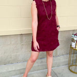 Sleeveless mini dress in rich garnet with 3D floral appliqué, scalloped embroidered hem, and side pockets. Elegant, textured, and perfect for fall or Gameday.