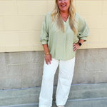 Sage green V-neck loose-fit blouse with pleated cuffed sleeves, styled for a fresh and effortless look.