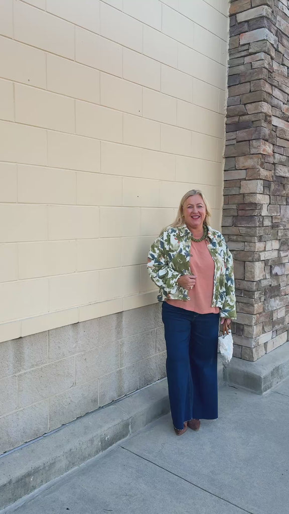 Painted Woodland Jacket featuring an olive, green, blue, and orange botanical print on a white background, a collared neckline, loop button closures, long sleeves, side pockets, and a cropped boxy silhouette.