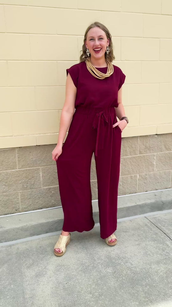 Garnet short-sleeve jumpsuit with elastic waist, front tie, high scoop neckline, and side pockets. Sporty, flattering, and perfect for Gameday style.