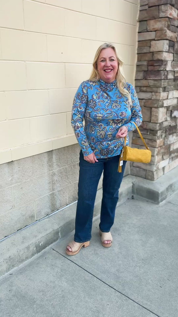 Baby blue long-sleeve top with a high neckline and geometric floral designs in yellow, green, and burgundy with decorative swirls.