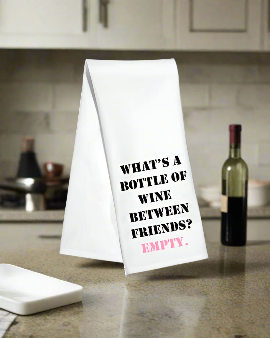 White kitchen towel with the phrase “What’s a bottle of wine between friends? Empty!”